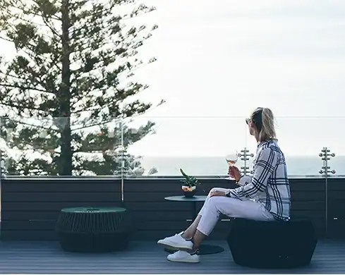 Modern woman relaxing outdoors on patio with drink and laptop, enjoying a peaceful break.