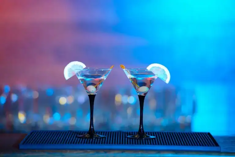 Cocktail glasses with lemon slices on bar counter at night.