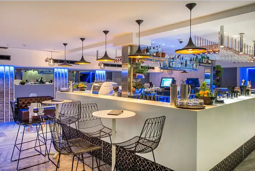 Modern bar interior with sleek design and stylish wire chairs, illuminated by pendant lighting.