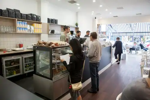 Cozy cafe interior with customers ordering food and drinks at the counter, modern décor and bright atmosphere.