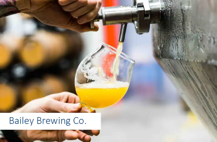 Brewery equipment and glass of freshly poured beer, close-up of beer tapping process in a brewery.
