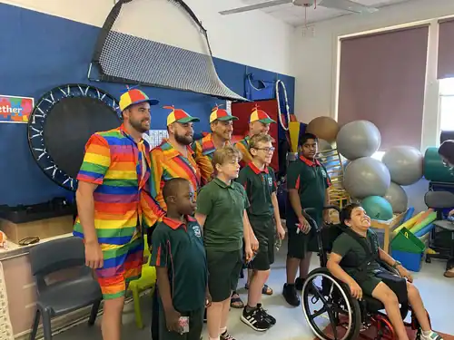 Rainbow-colored performers entertaining children in a therapy or activity room.