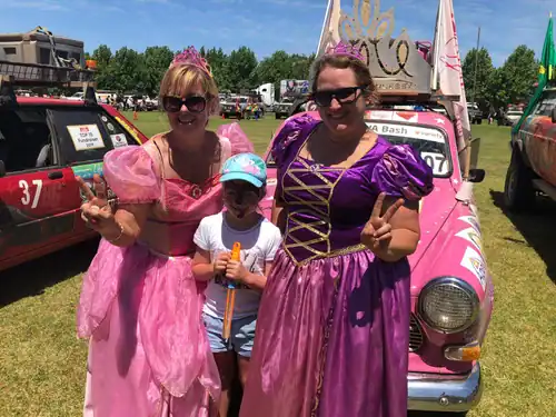 Colorful princess costumes at a fun outdoor event with a pink vintage car.