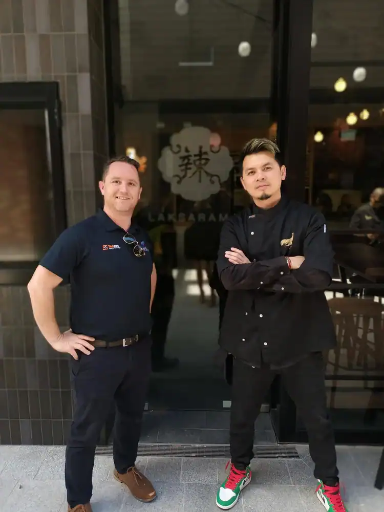 Professional men standing outside the restaurant entrance, smiling and posing confidently, modern urban setting, diverse staff, casual and stylish attire.