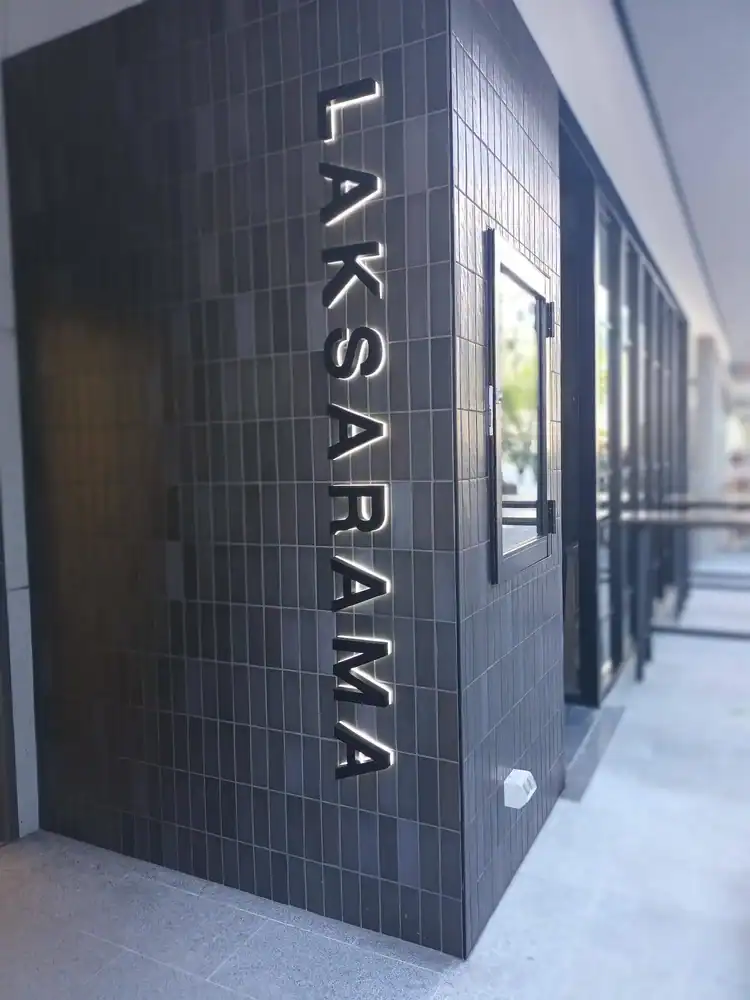 97 characters, black tile exterior with illuminated "LAKSARA" sign. Modern building facade with outdoor area and large windows.