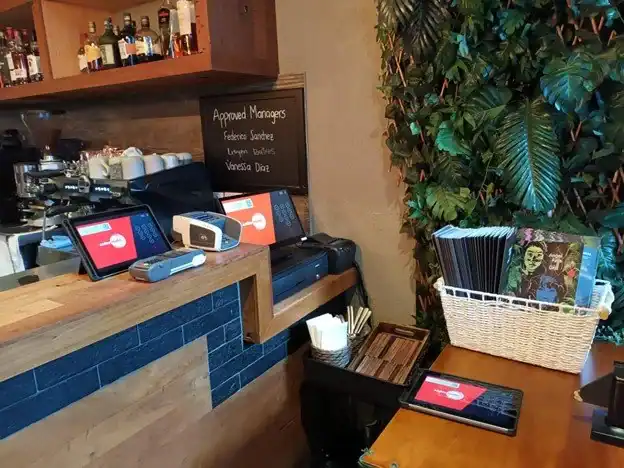 Flexible point-of-sale devices on a wooden café counter with digital ordering screens and a payment swiper.