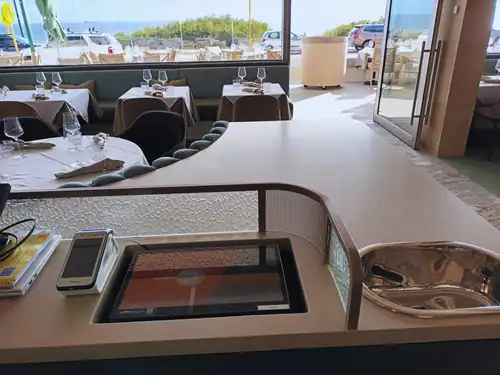 Modern restaurant interior with table settings and large windows overlooking outdoor seating area.