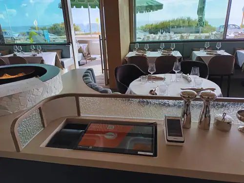 Modern restaurant table setup with glassware and napkins overlooking an outdoor patio scene.