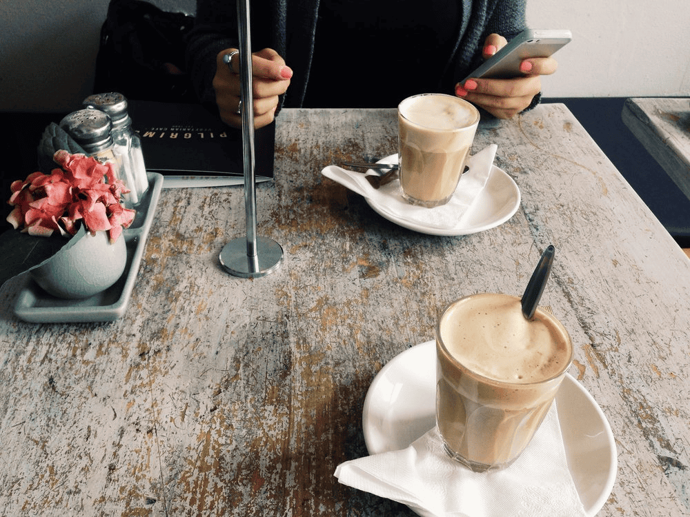Coffee drinks on a wooden table with a person using a smartphone.