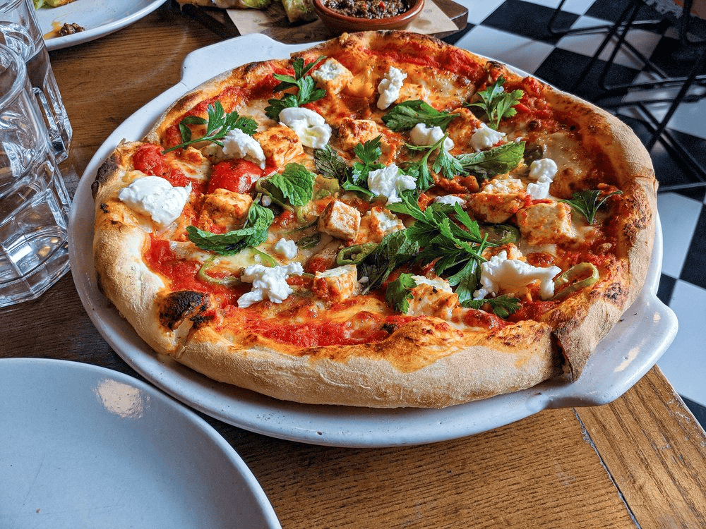 Fresh veggie and chicken pizza with feta cheese on a wooden table at a restaurant.