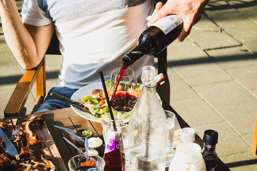 Bottle of red wine being poured into a glass at an outdoor dining table.
