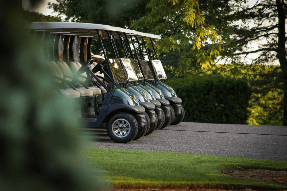 Golf carts parked on golf course fairway, outdoor golf equipment, sunny day, lush green trees, golf course landscape.