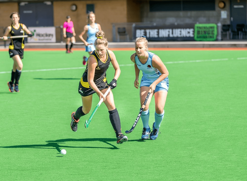 Field hockey game with female players in action on green turf.