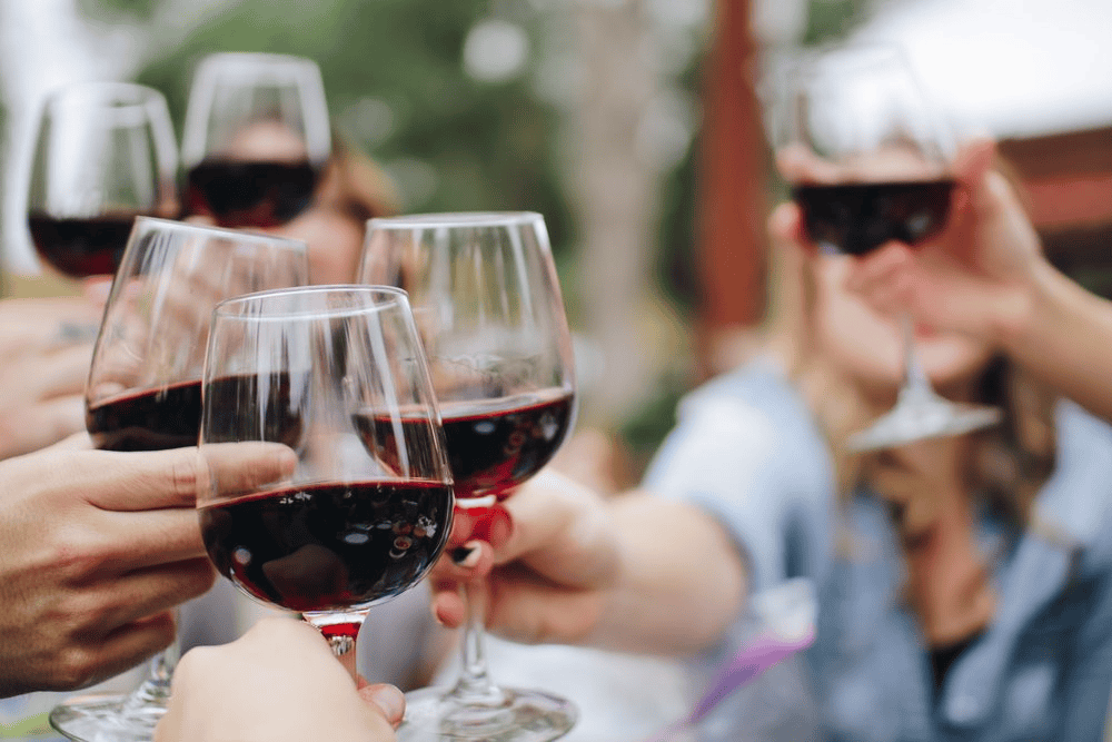 Glasses of red wine toasting outdoors at a social gathering.