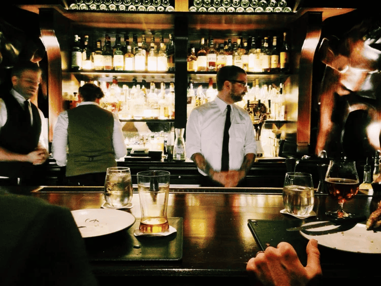 Modern bar with bartenders preparing drinks in a stylish setting with liquor bottles in the background.
