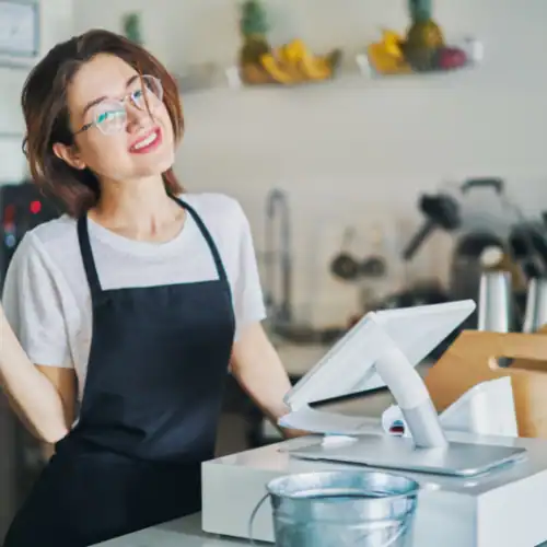 Food service worker smiling at register in cafe or restaurant setting.