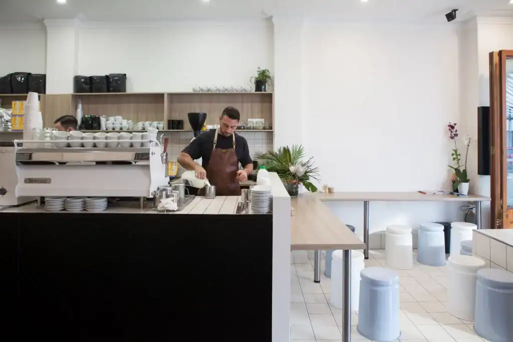 Coffee shop barista preparing drinks in a modern café, showcasing professional coffee equipment and clean interior.