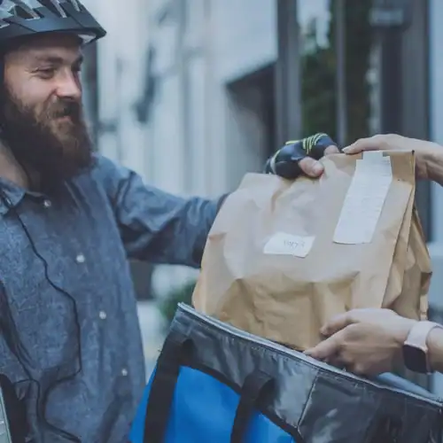 Delivery person handing over a package outside an office building during a delivery.