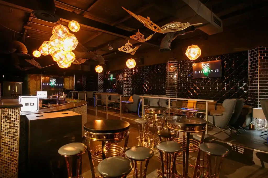 Luxury bar interior with copper tables and modern lighting, stylish seating, and decorative wall accents at Butterfly 73 nightclub.