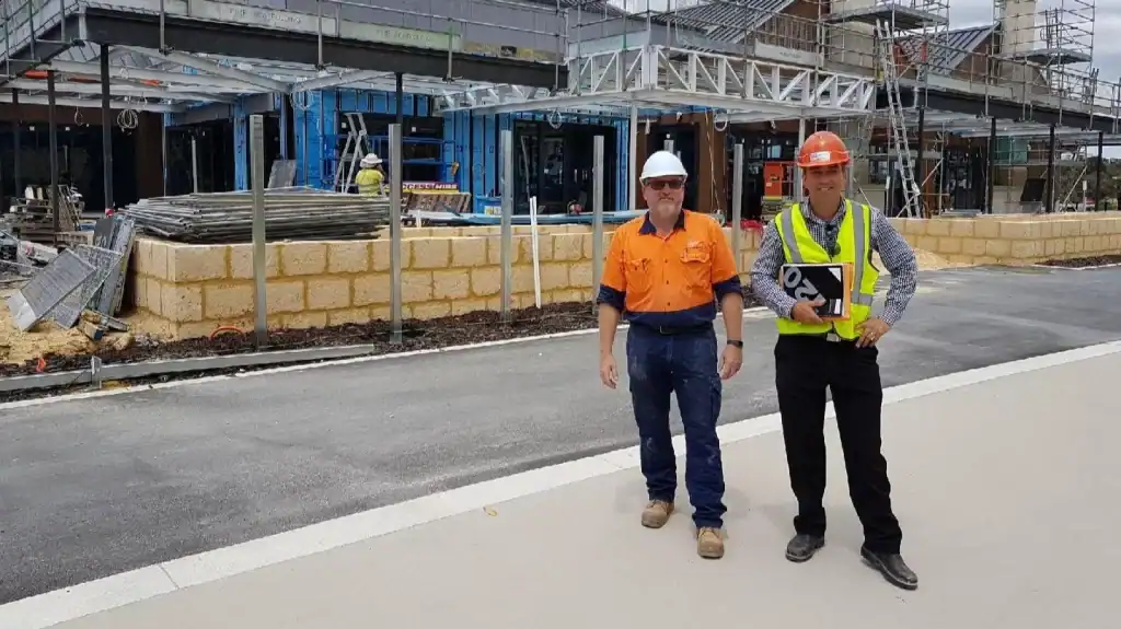 Construction site with two workers wearing safety gear and building materials in progress.