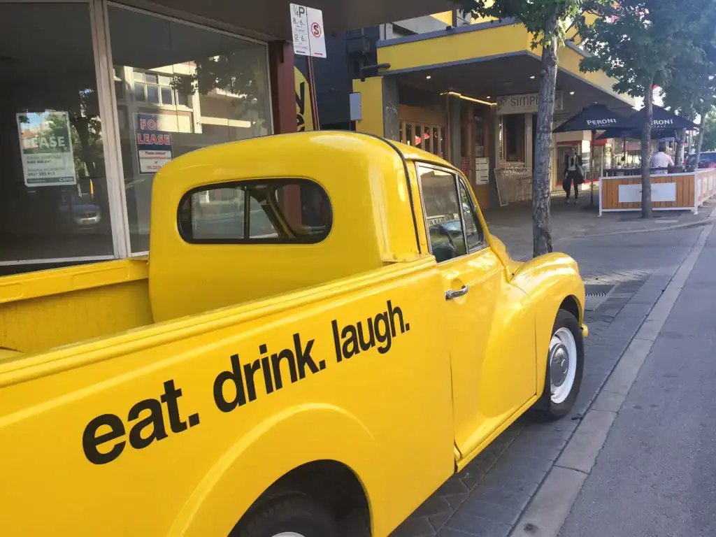 Yellow vintage truck parked on city street with "eat. drink. laugh." text on the side.
