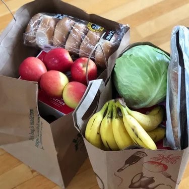 Fresh apples, bananas, cabbage, and bread in paper grocery bags for grocery shopping.