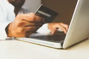 Modern person holding credit card at laptop for online transaction.