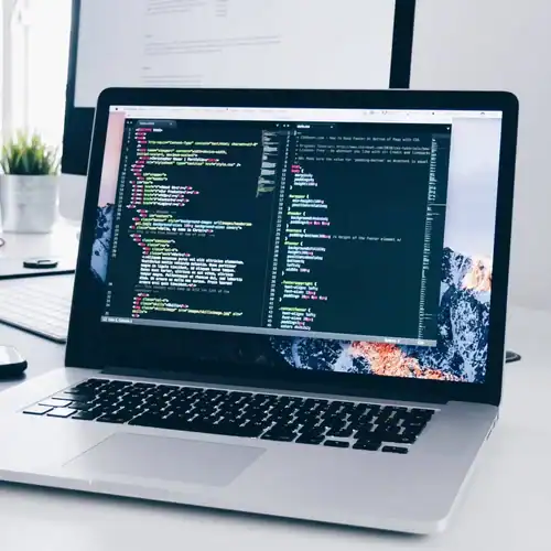 Laptop displaying coding on screen, connected to renewable energy sources, in a modern office environment.