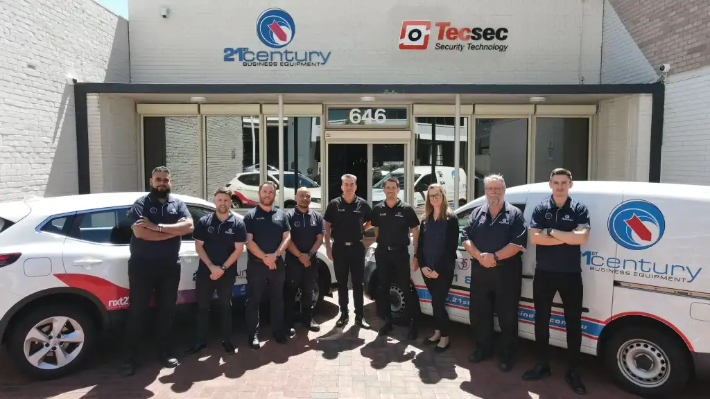 Professional team of 21st Century Business Equipment staff standing outside the company office with branded vehicles.