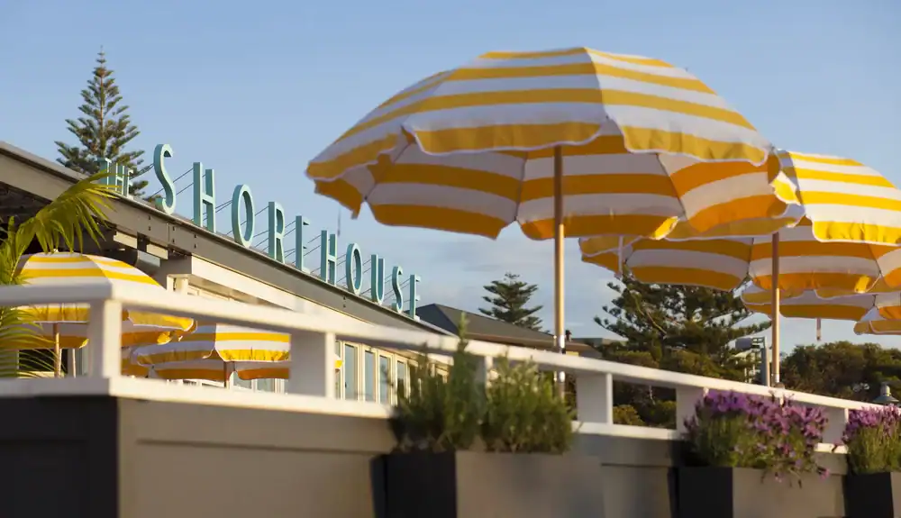 Yellow and white striped umbrellas on an outdoor patio with a building in the background and "SHOREHOUSE" sign.