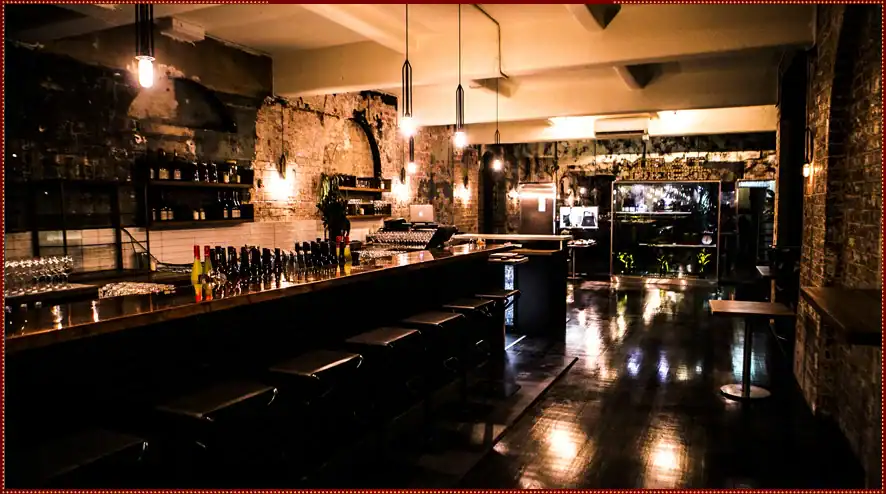 Cozy industrial-style bar with exposed brick walls, ambient lighting, and modern furnishings.