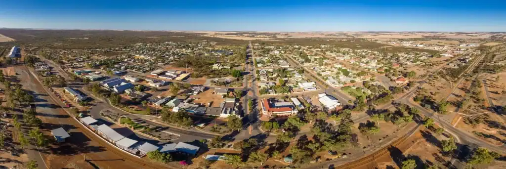 Drone view of a suburban town with residential houses, commercial buildings, and greenery in a dry landscape.