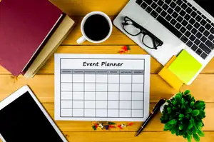 Event planner calendar on wooden desk with office supplies and a laptop for business organization.