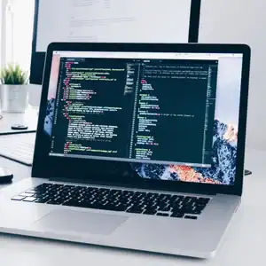 High-tech laptop displaying coding and software development on a modern desk setup.