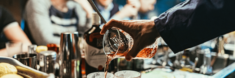 Pouring cocktails into glasses at a bar scene.