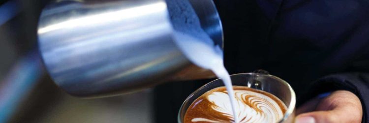 Coffee machine pouring milk into latte.