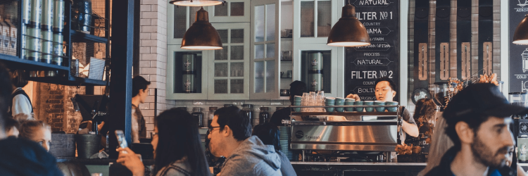 Coffee shop interior with customers and baristas, cozy cafe ambiance with hanging lights and menu boards.